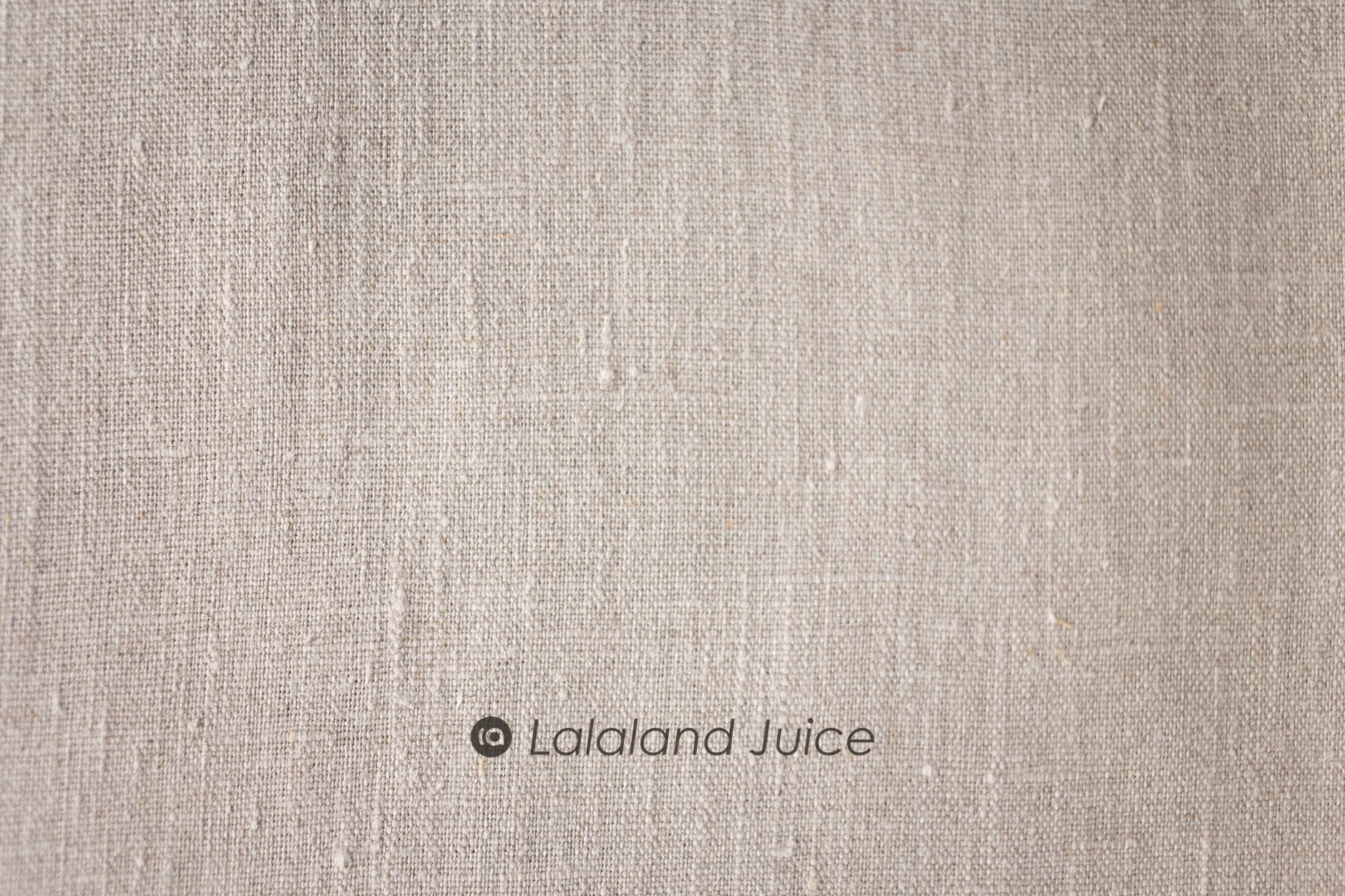 Neutral linen in macro — the weave, the slubs, the quiet — with the Lalaland Juice mark set within.